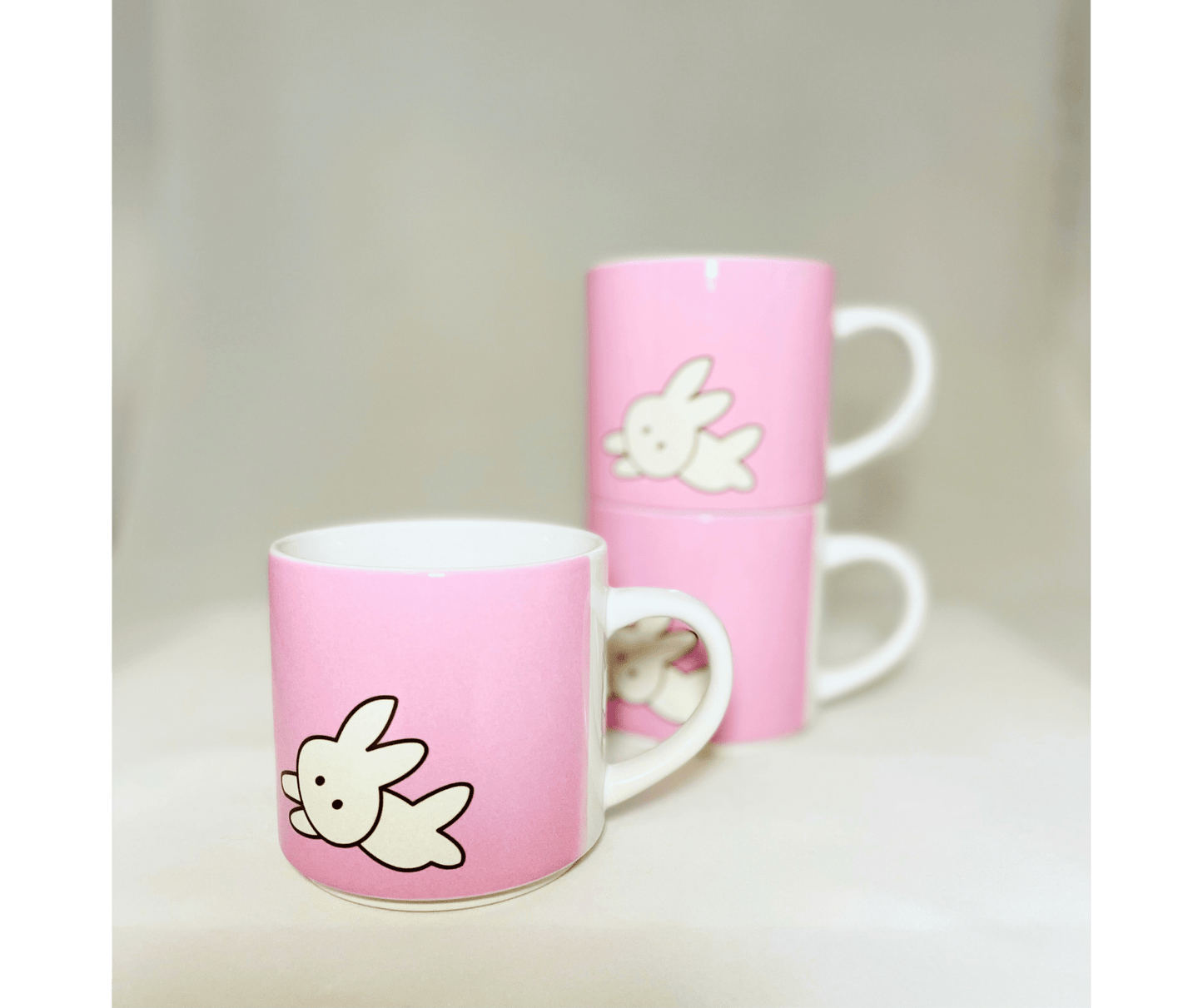 kawaii bunny mugs. 3 pink stackable 10 oz coffee mugs in front of a flower on white background