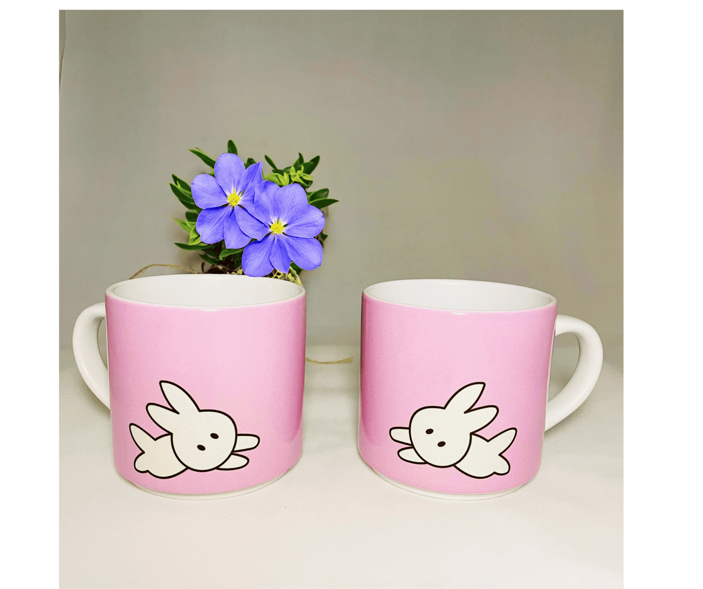kawaii bunny mugs. 2 pink stackable 10 oz coffee mugs in front of a flower on white background